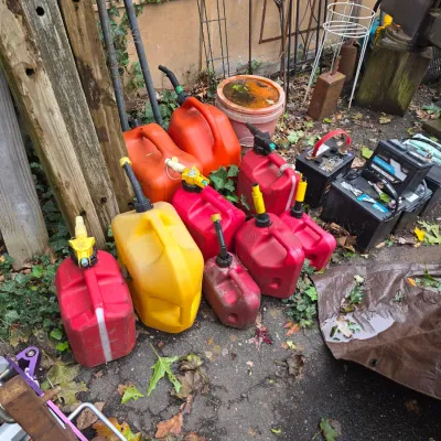 Sale Photo Thumbnail #59: Assortment of used plastic gas cans in red, yellow, and orange, alongside several automotive batteries.