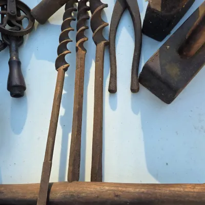 Sale Photo Thumbnail #31: Collection of antique hand tools, including rusty auger drill bits, a hand drill, pliers, and wooden hand planes.