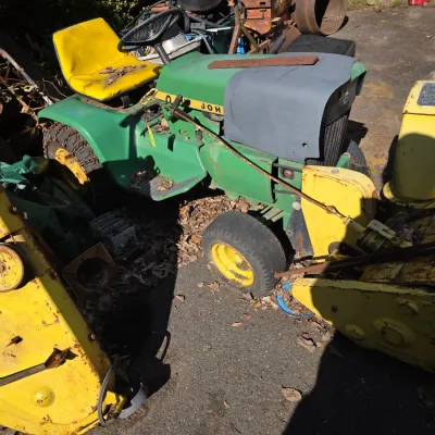 Sale Photo Thumbnail #41: Vintage John Deere lawn tractor with a yellow snowblower attachment and a separate yellow mower deck, showing significant wear and rust.