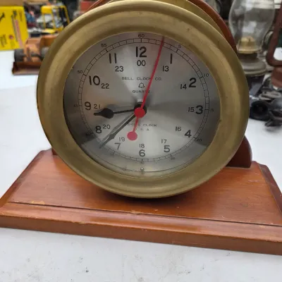 Sale Photo Thumbnail #56: Bell Clock Co. quartz ship's clock with a brass bezel, mounted on a wooden base.