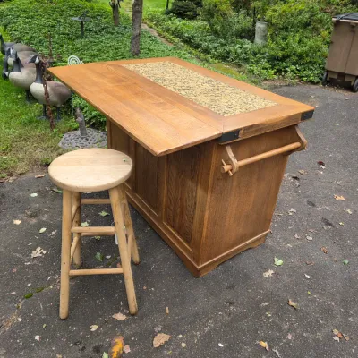 Sale Photo Thumbnail #51: Oak kitchen island with a 12 inch drop-leaf extension, tiled top inlay, and side towel bar, paired with a simple round wooden bar stool.