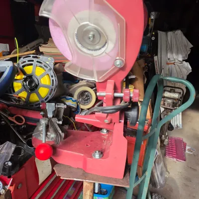 Sale Photo Thumbnail #57: Red electric chainsaw sharpener with a clear safety guard, mounted on a metal stand in a workshop setting.