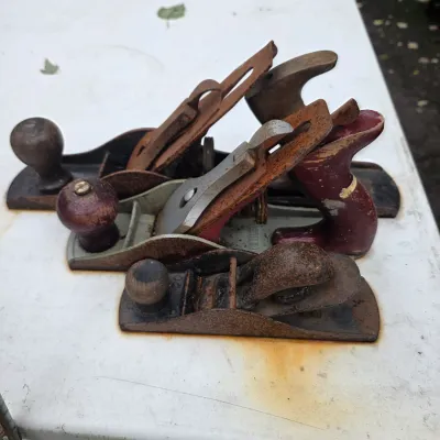 Sale Photo Thumbnail #60: Three vintage hand planes of varying sizes, showing significant rust and wear on the metal bodies and wooden handles.