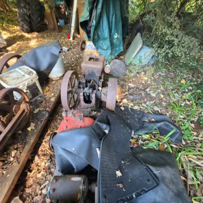 Sale Photo Thumbnail #4: Vintage hit-and-miss stationary engine with heavy rust and wear, stored outdoors alongside other antique machinery parts.