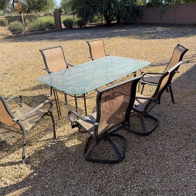 Sale Photo Thumbnail #239: Outdoor dining set featuring a rectangular glass-top table with a metal frame and six matching mesh sling chairs, including swivel rocker styles.