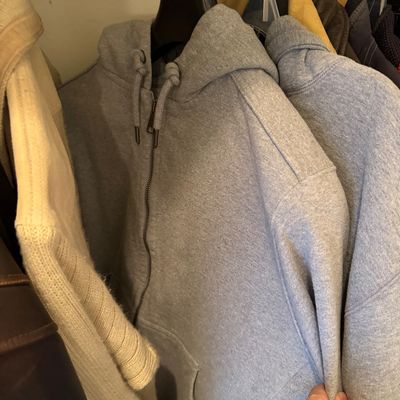 Sale Photo Thumbnail #182: Grey zip-up hooded sweatshirt hanging in a closet alongside other outerwear.