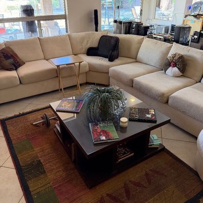 Sale Photo Thumbnail #282: Large beige sectional sofa paired with a dark wood square coffee table featuring a glass top, set over an earth-toned patterned area rug.