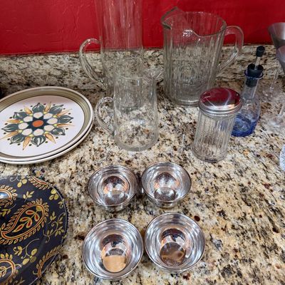 Sale Photo Thumbnail #217: Assorted kitchenware including three clear glass pitchers, a sugar shaker, four small metal bowls, and patterned ceramic plates.