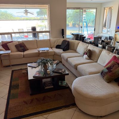 Large contemporary cream-colored sectional sofa with a curved chaise end, paired with a dark wood and glass coffee table on a patterned...