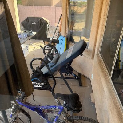 Mongoose full suspension mountain bike in blue and silver, shown alongside an inversion table on a covered patio.