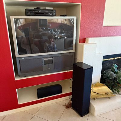 Vintage Hitachi rear-projection television paired with a DVD/VCR player, a center channel speaker, and a black tower speaker, circa early...
