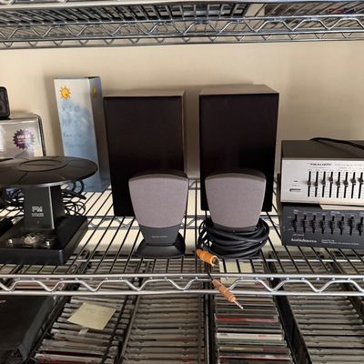 Harman Kardon computer speakers, a pair of black bookshelf speakers, and audio components displayed on a wire shelf above racks of CDs.