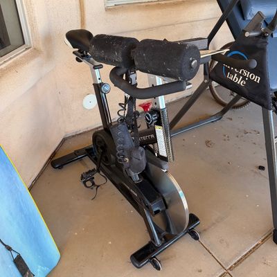 Sale Photo Thumbnail #227: Xterra stationary exercise bike with a heavy flywheel, adjustable seat, and foam-padded handlebars, shown alongside an Ironman inversion table.