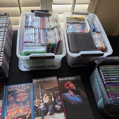 Collection of music CDs in plastic storage bins and cases, featuring box sets from Little Feat, The Allman Brothers Band, and Marvin Gaye.