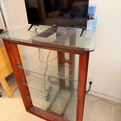Sale Photo Thumbnail #141: Modern Onn flat-screen television sitting atop a cherry-finished wood and glass media tower with multiple shelves.