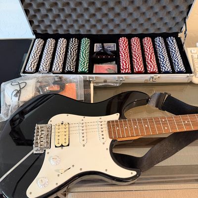 Sale Photo Thumbnail #291: Black electric guitar with a white pickguard and strap, displayed alongside a complete poker chip set in an aluminum carrying case.