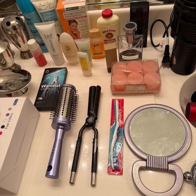 Sale Photo Thumbnail #164: Assortment of personal care and beauty items, including a purple round brush, a hair crimper, a hand mirror, a packaged toothbrush, and various lotions and toiletries.