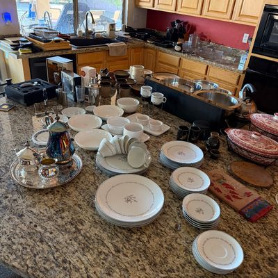 Assorted kitchenware and dining items displayed on a granite kitchen island, including a silver-plated tea service, white porcelain...