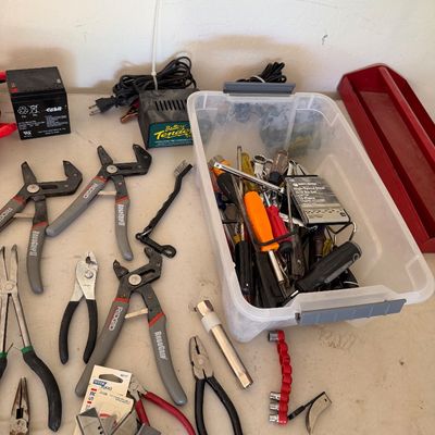 Assorted hand tools including RoboGrip pliers, wire cutters, a Battery Tender charger, and a plastic bin filled with screwdrivers and...