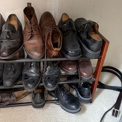 Sale Photo Thumbnail #134: Assorted men's leather dress shoes and boots, including loafers, oxfords, and chukka boots, displayed on a three-tier metal and wood shoe rack.