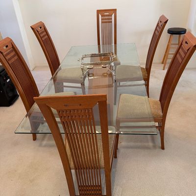 Sale Photo Thumbnail #308: Modern dining set featuring a rectangular glass-top table with a wooden base and six matching high-back wooden chairs with upholstered seats.