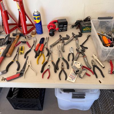 Assorted hand tools including pliers, wire cutters, and a hammer, displayed alongside jack stands, a Battery Tender, and a can of WD-40...