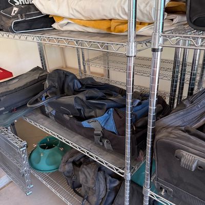 Assorted luggage, duffel bags, and a Shoei helmet bag stored on chrome wire shelving units.