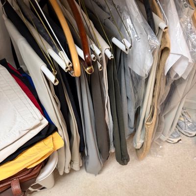 Sale Photo Thumbnail #123: Assortment of men's trousers and slacks hanging on hangers in a closet, alongside folded garments in a laundry basket.