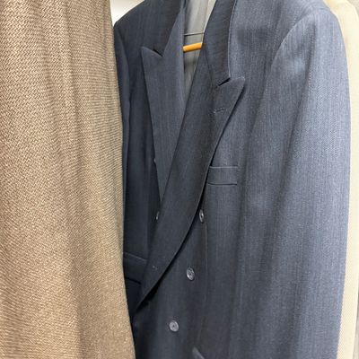 Sale Photo Thumbnail #117: Vintage double-breasted charcoal grey pinstripe suit jacket hanging in a closet alongside other men's blazers.