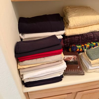 Sale Photo Thumbnail #175: Assorted bed linens, blankets, and towels stacked on a counter, including a packaged Hotel Collection item.