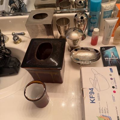 Sale Photo Thumbnail #163: Assorted bathroom accessories including a silver-tone tissue box cover, matching metal cups, a brown ceramic tissue box cover, and various personal care items.