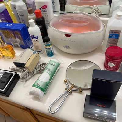 Sale Photo Thumbnail #131: Assorted personal care and beauty items, including a Remington paraffin bath, a hand mirror, cotton rounds, and various hair and skin care products.
