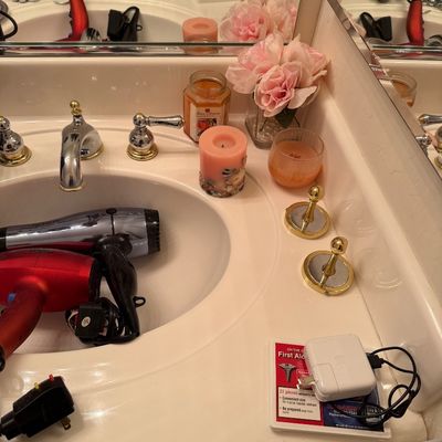 Sale Photo Thumbnail #168: Assorted bathroom vanity items including hair dryers, decorative candles, faux pink flowers, and electronic chargers.
