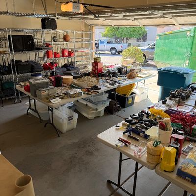 Assorted garage sale items including hand tools, painting supplies, storage bins, and wire shelving units arranged on folding tables.