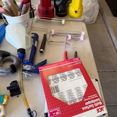 Assorted home improvement and painting supplies, including paint rollers, brushes, a caulk gun, flashlights, and a package of Ace...