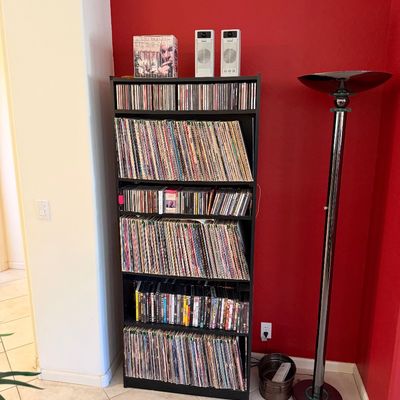 Sale Photo Thumbnail #294: Black laminate media shelving unit filled with vinyl records, CDs, and DVDs, shown next to a chrome halogen torchiere floor lamp.