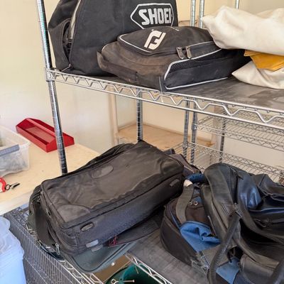 Assorted travel and gear bags, including a Shoei helmet bag and a FootJoy shoe bag, displayed on wire shelving.