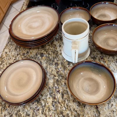 Sale Photo Thumbnail #191: Mid-century modern style stoneware dinnerware set featuring a brown and beige glazed finish, including plates, bowls, and a ceramic mug.