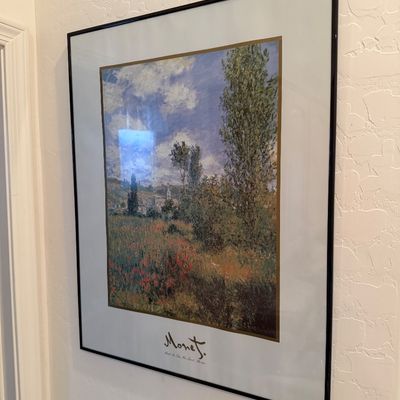 Sale Photo Thumbnail #170: Framed Claude Monet exhibition poster featuring a landscape print with a field of poppies, housed in a simple black metal frame with a wide white mat.