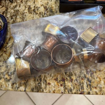 Sale Photo Thumbnail #206: Collection of vintage metal napkin rings in copper and brass tones, packaged in a clear plastic bag.