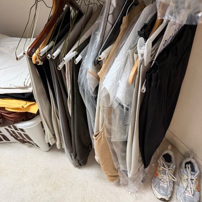 Sale Photo Thumbnail #124: Assorted men's trousers and slacks hanging in a closet, some protected by dry cleaning plastic, alongside a pair of athletic sneakers.