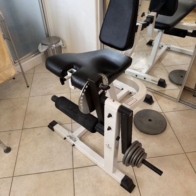 Sale Photo Thumbnail #139: TuffStuff plate-loaded leg extension and curl machine with white steel frame and black vinyl padding, shown with several weight plates.