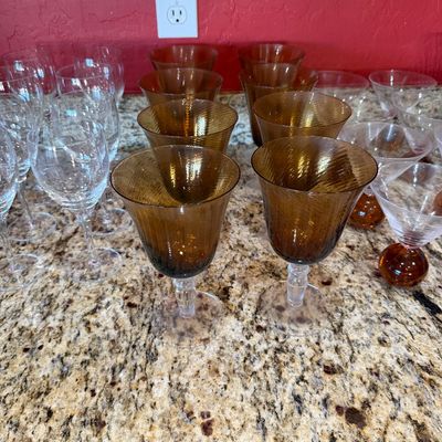 Sale Photo Thumbnail #209: Assortment of vintage glassware, featuring amber-colored textured goblets with clear stems alongside clear wine glasses and martini glasses with amber bubble bases.