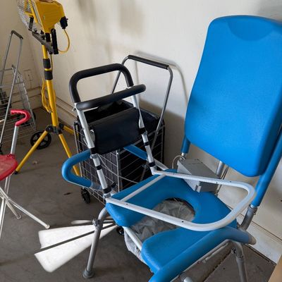 Sale Photo Thumbnail #111: Blue padded shower commode chair with adjustable frame, shown alongside a rolling utility cart and a yellow tripod work light.