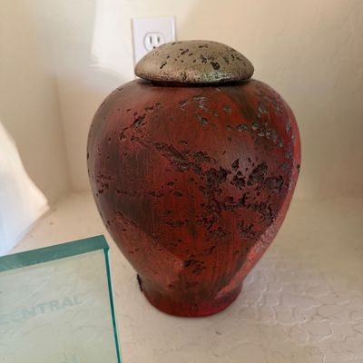 Sale Photo Thumbnail #273: Rustic ceramic lidded jar with a textured, distressed red and black finish and a metallic silver-toned lid.