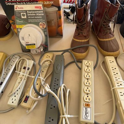 Sale Photo Thumbnail #101: Assortment of household items including multiple power strips, a Kidde replacement smoke alarm in original packaging, a boxed Vitamin Bar deluxe juicer, and a pair of Sorel-style winter boots.