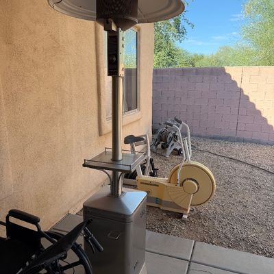 Sale Photo Thumbnail #248: Stainless steel outdoor patio heater with a built-in drink tray, shown alongside a vintage Tunturi exercise bike and other outdoor items.