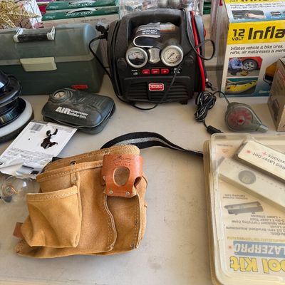 Assorted tools and garage items, including a suede leather tool pouch, a portable jump starter and tire inflator, and a boxed 12-volt...