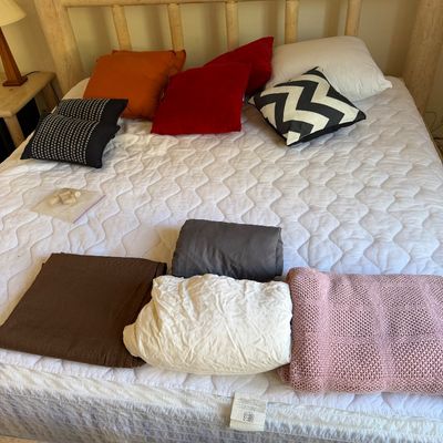 Sale Photo Thumbnail #184: Rustic log-style wooden bed frame with mattress, featuring an assortment of colorful throw pillows and folded blankets.