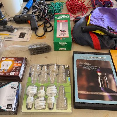 Assorted household items and tools, including light bulbs, a Black & Decker power drill, a Fluidmaster flush valve, and various ropes...